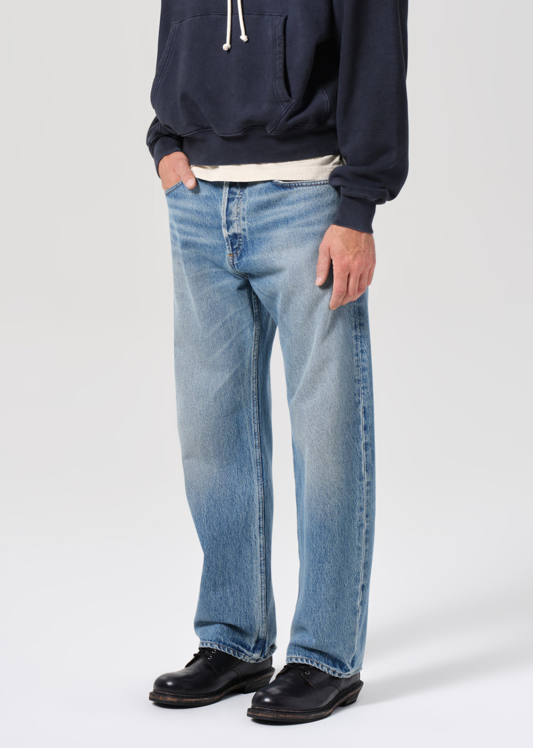 Person wearing a navy hoodie, light blue jeans, and black shoes on a white background