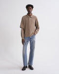 Man wearing a beige polo shirt and blue jeans on a white background