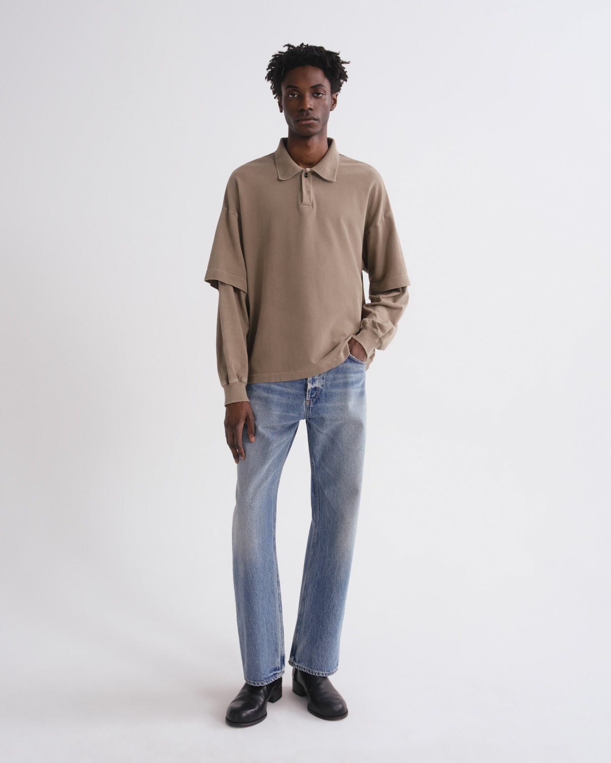 Man wearing a beige polo shirt and blue jeans on a white background