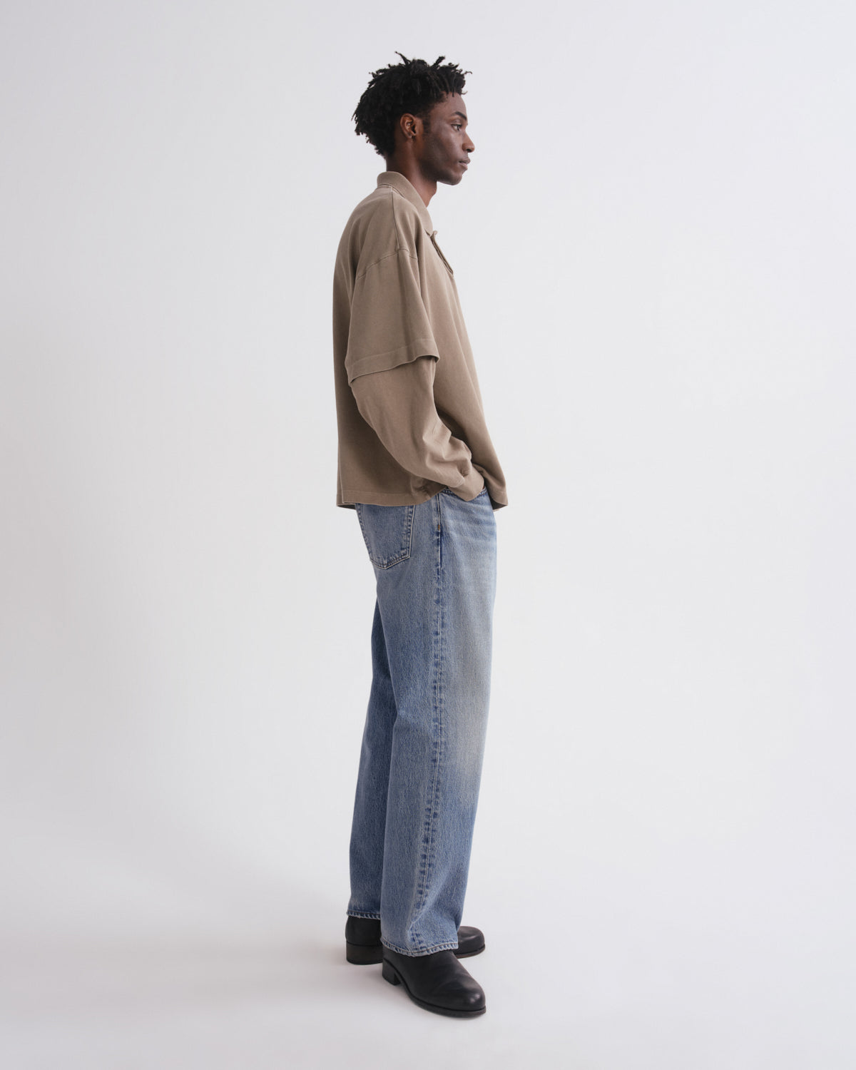 Person wearing a beige shirt and blue jeans standing against a white background