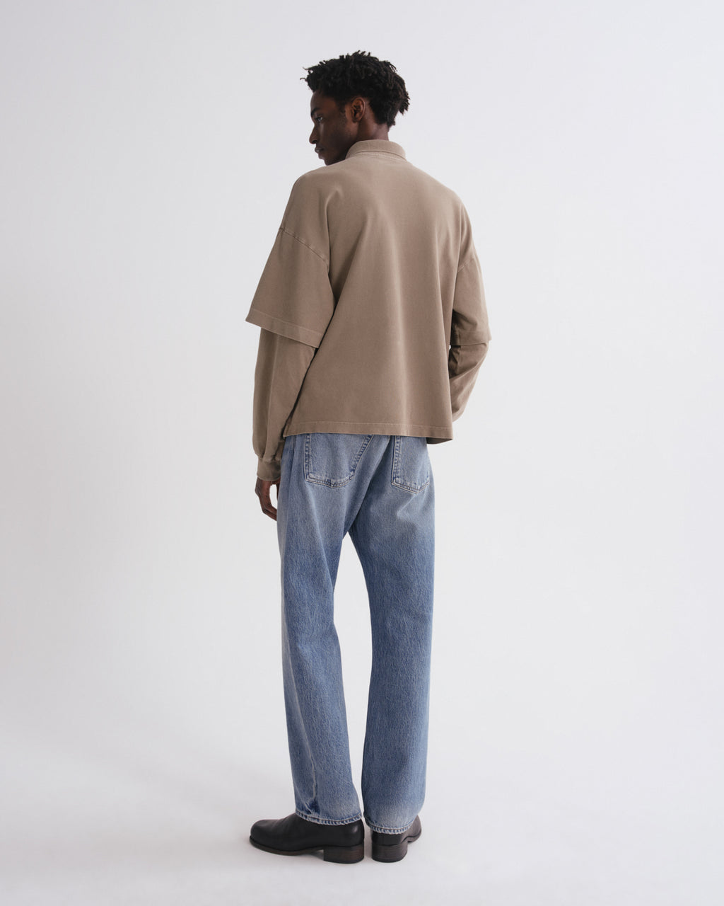 Person wearing a beige jacket and blue jeans on a white background
