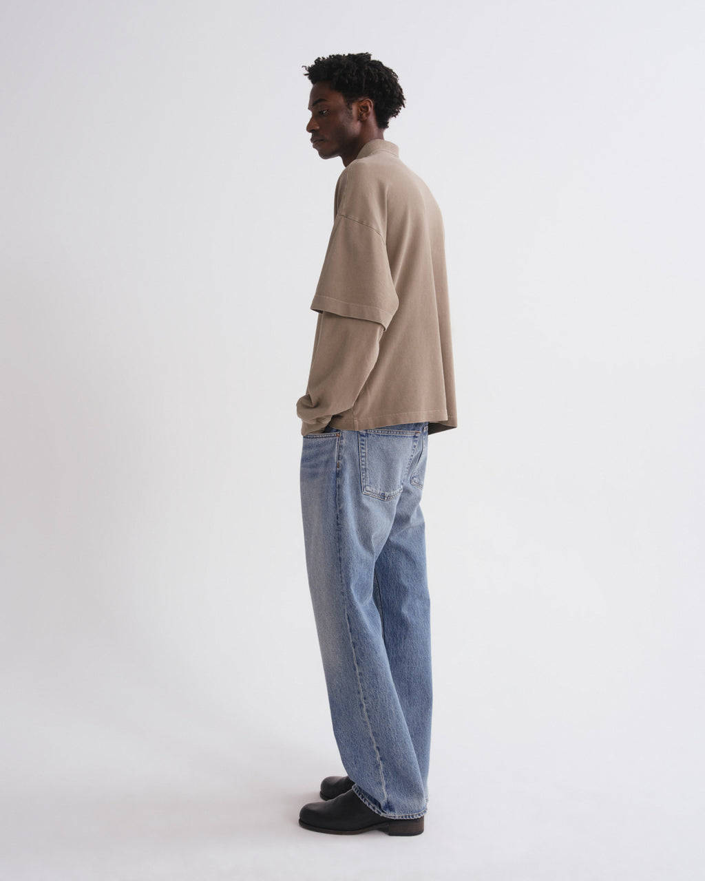 Person wearing a beige shirt and blue jeans on a white background