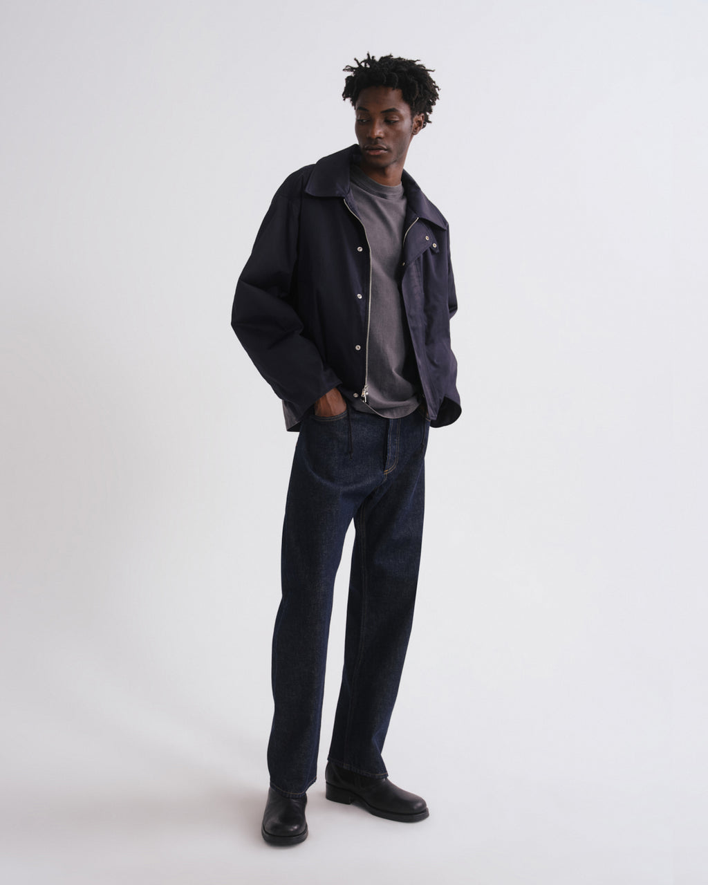 Person wearing a dark jacket, gray shirt, and jeans on a white background