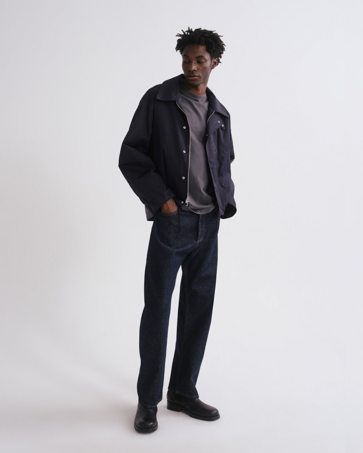 Person wearing a dark jacket, gray shirt, and jeans on a white background