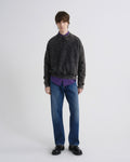 Person wearing a dark gray sweater, purple shirt, blue jeans, and black shoes on a white background