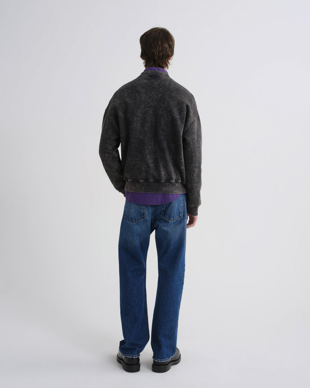 Person wearing a dark gray sweater and blue jeans on a white background