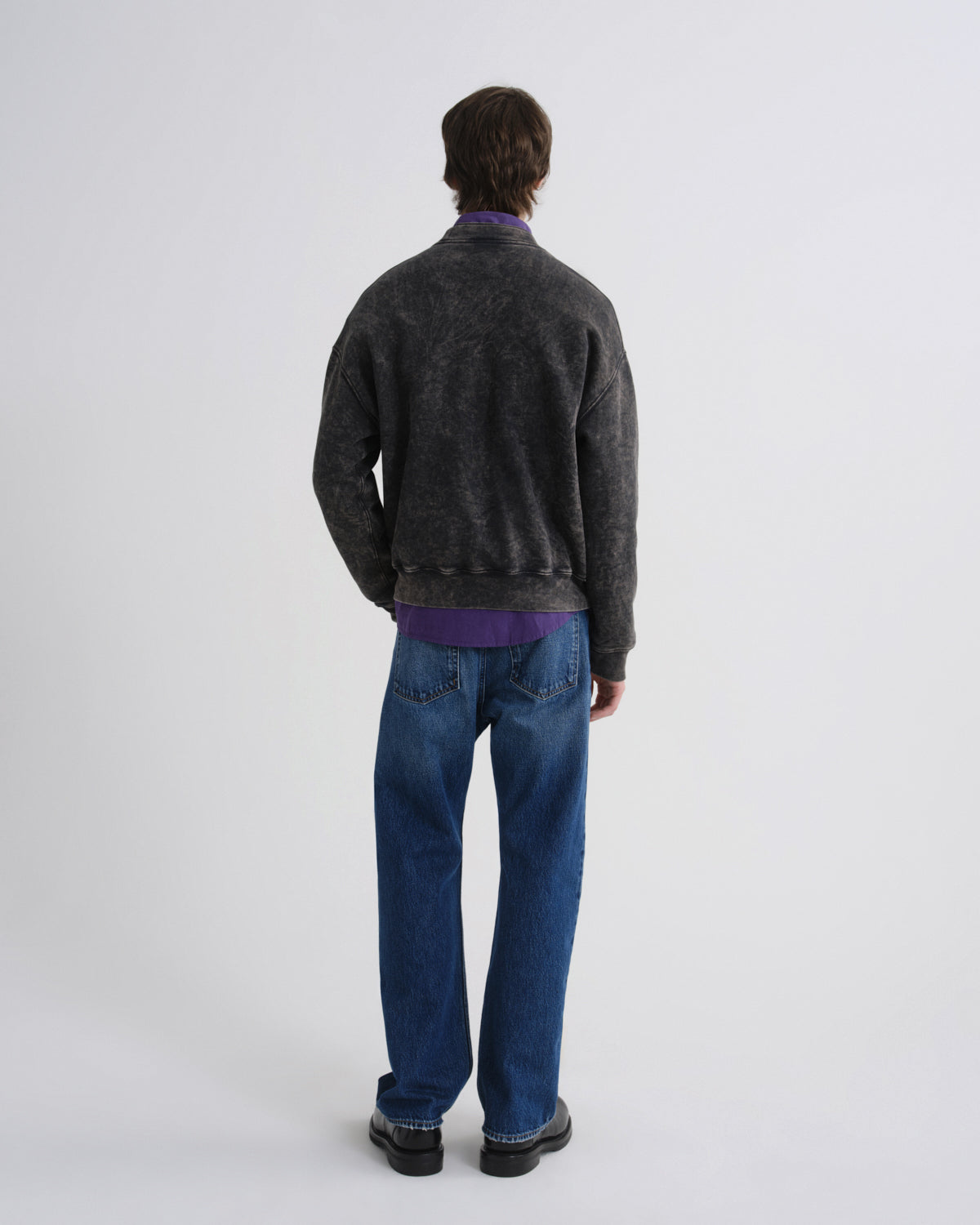Person wearing a dark gray sweater and blue jeans on a white background