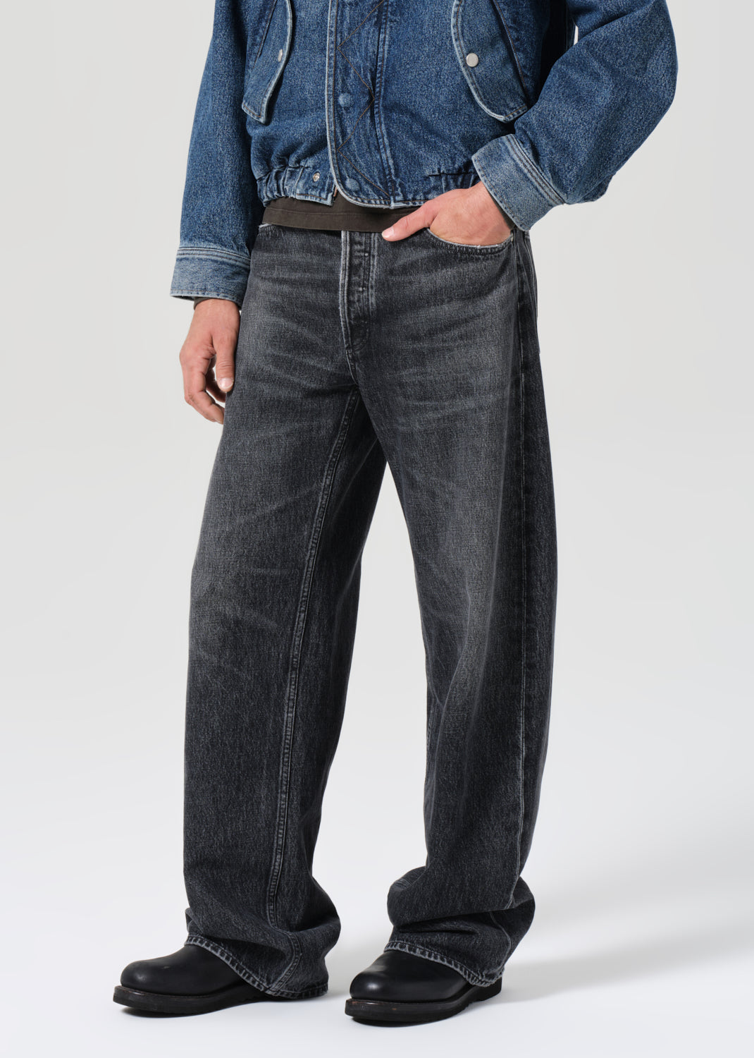 Person wearing a blue denim jacket and black jeans on a white background