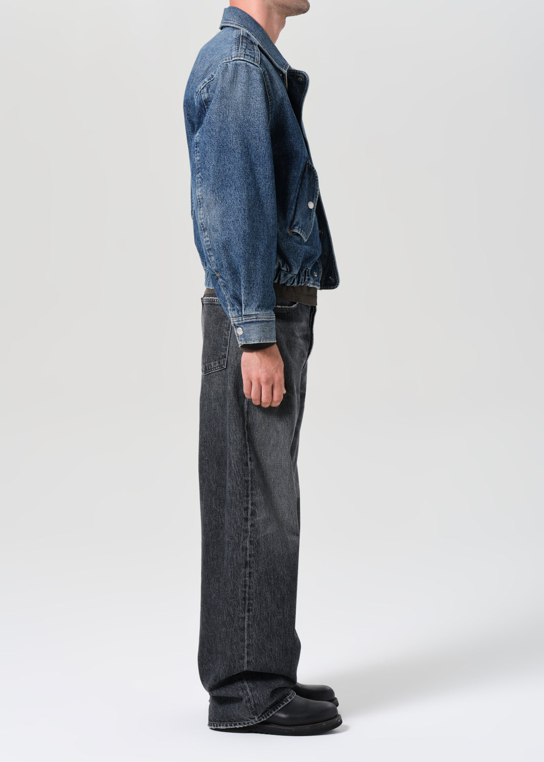 Person wearing a blue denim jacket and black jeans on a white background