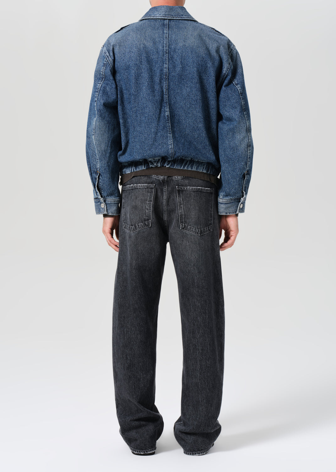 Person wearing a blue denim jacket and black jeans on a white background