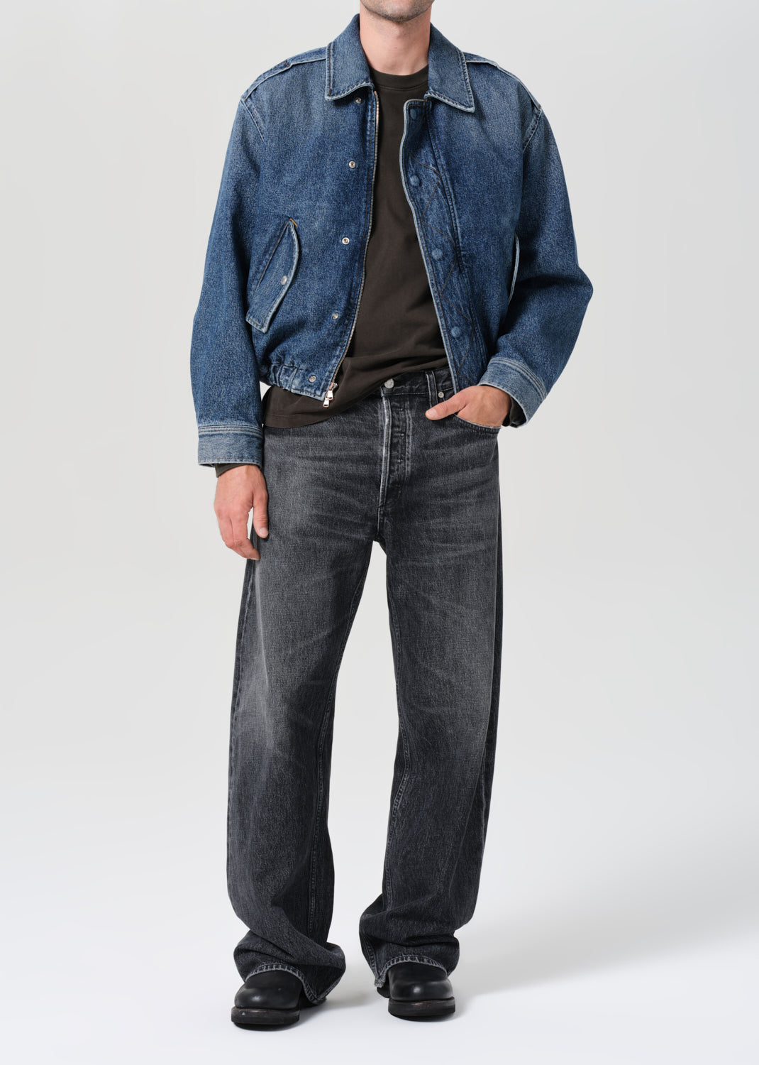 Person wearing a blue denim jacket and dark jeans on a white background