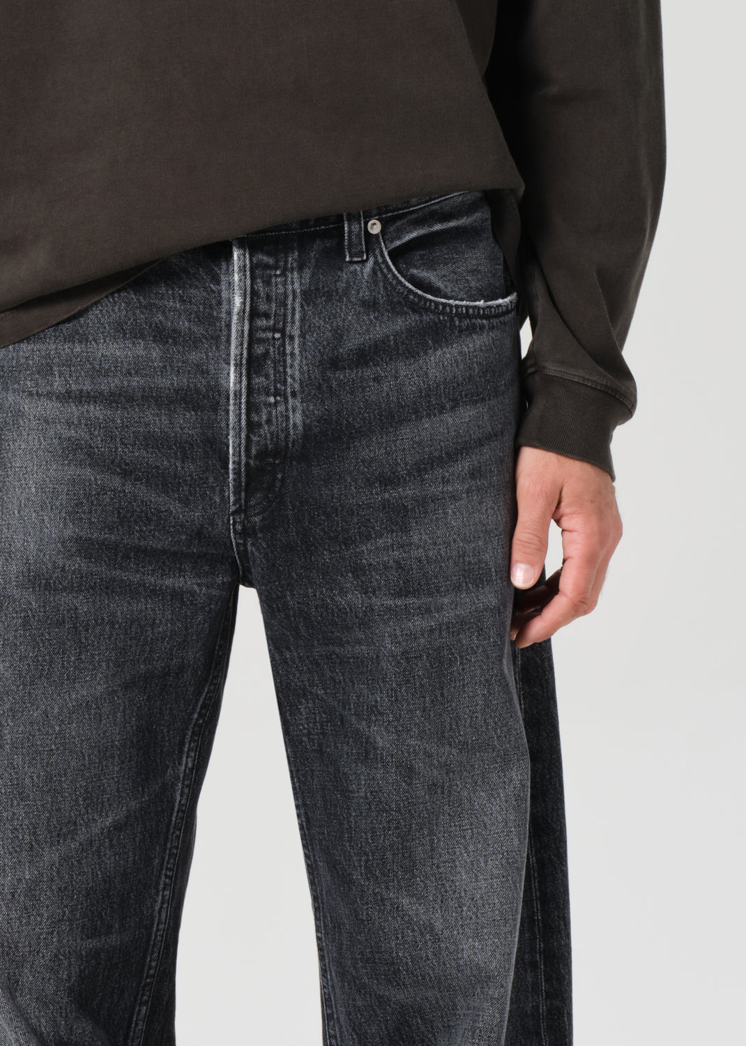 Person wearing dark gray jeans and a black long-sleeve shirt on a light gray background