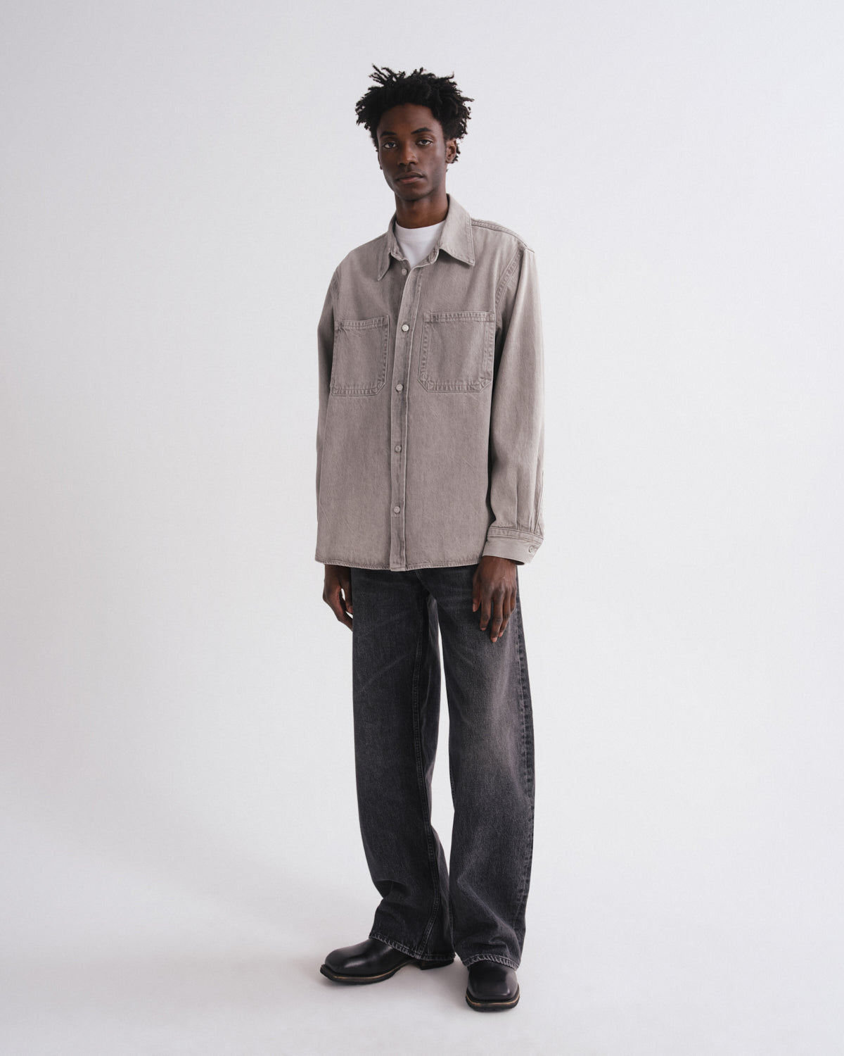 Person wearing a gray jacket and dark jeans on a white background