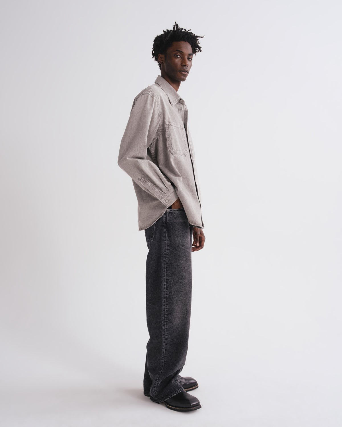 Man wearing a light gray shirt and dark jeans on a white background
