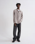 Man wearing a beige shirt and dark jeans on a white background