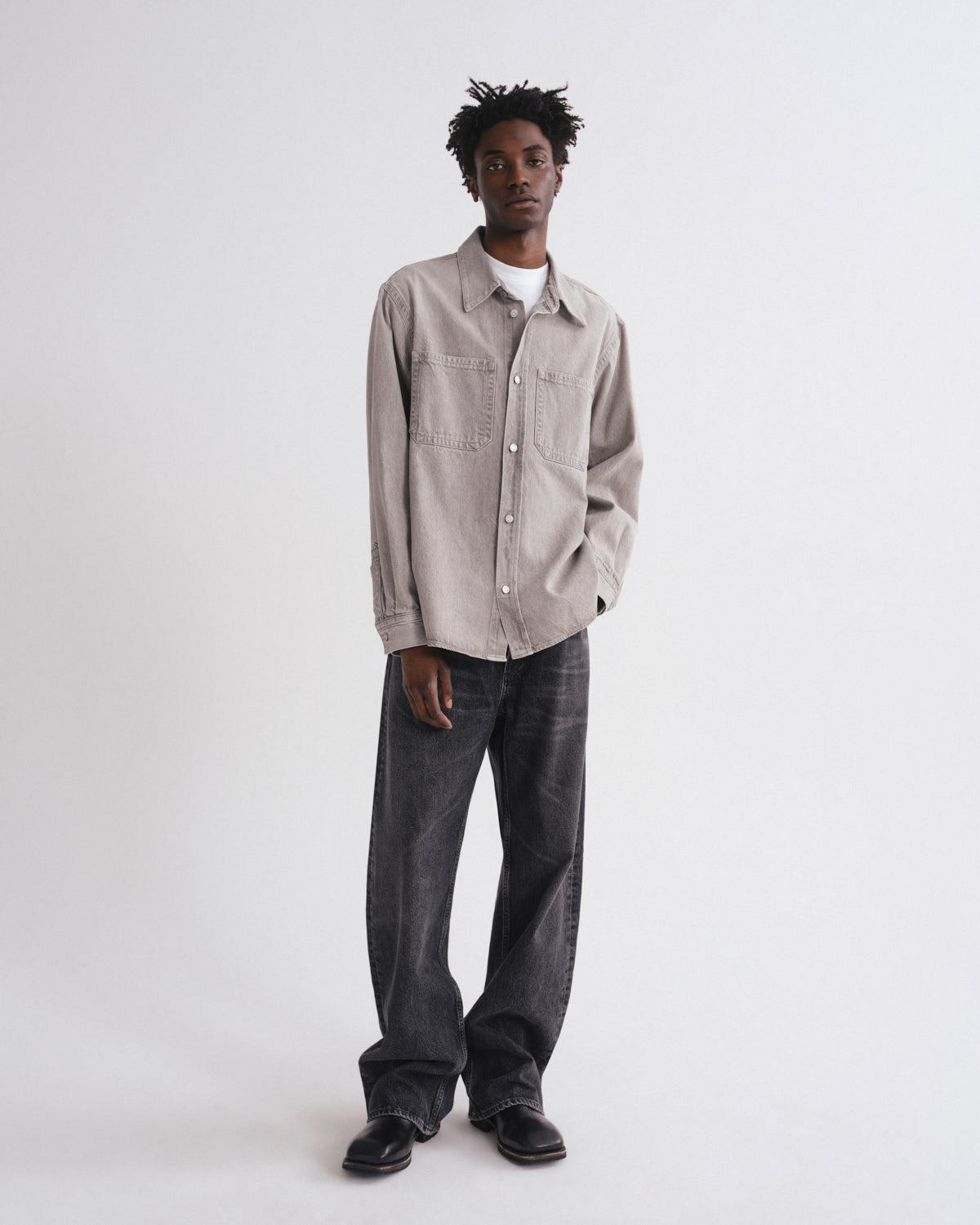 Man wearing a beige shirt and dark jeans on a white background