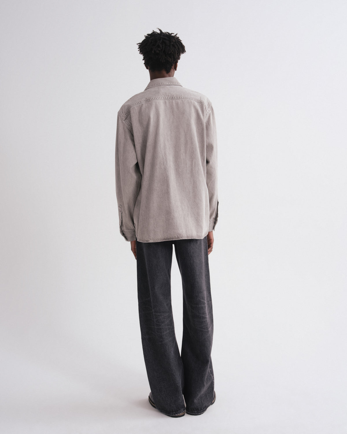Person wearing a light gray shirt and dark pants on a white background