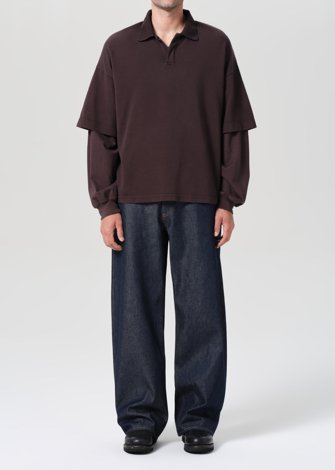 Person wearing a brown long-sleeve shirt and dark jeans on a white background