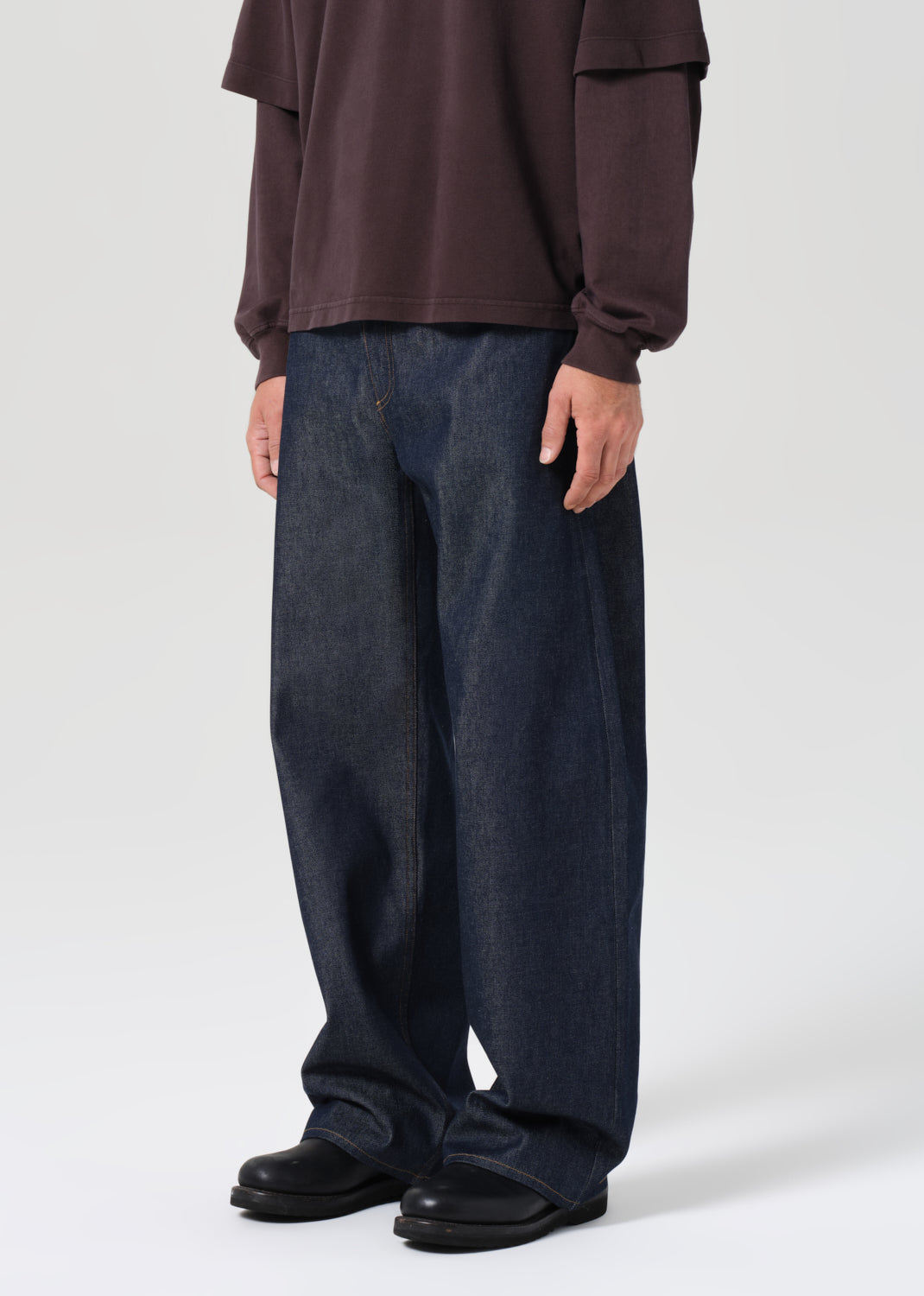 Person wearing a brown shirt and dark blue jeans on a white background