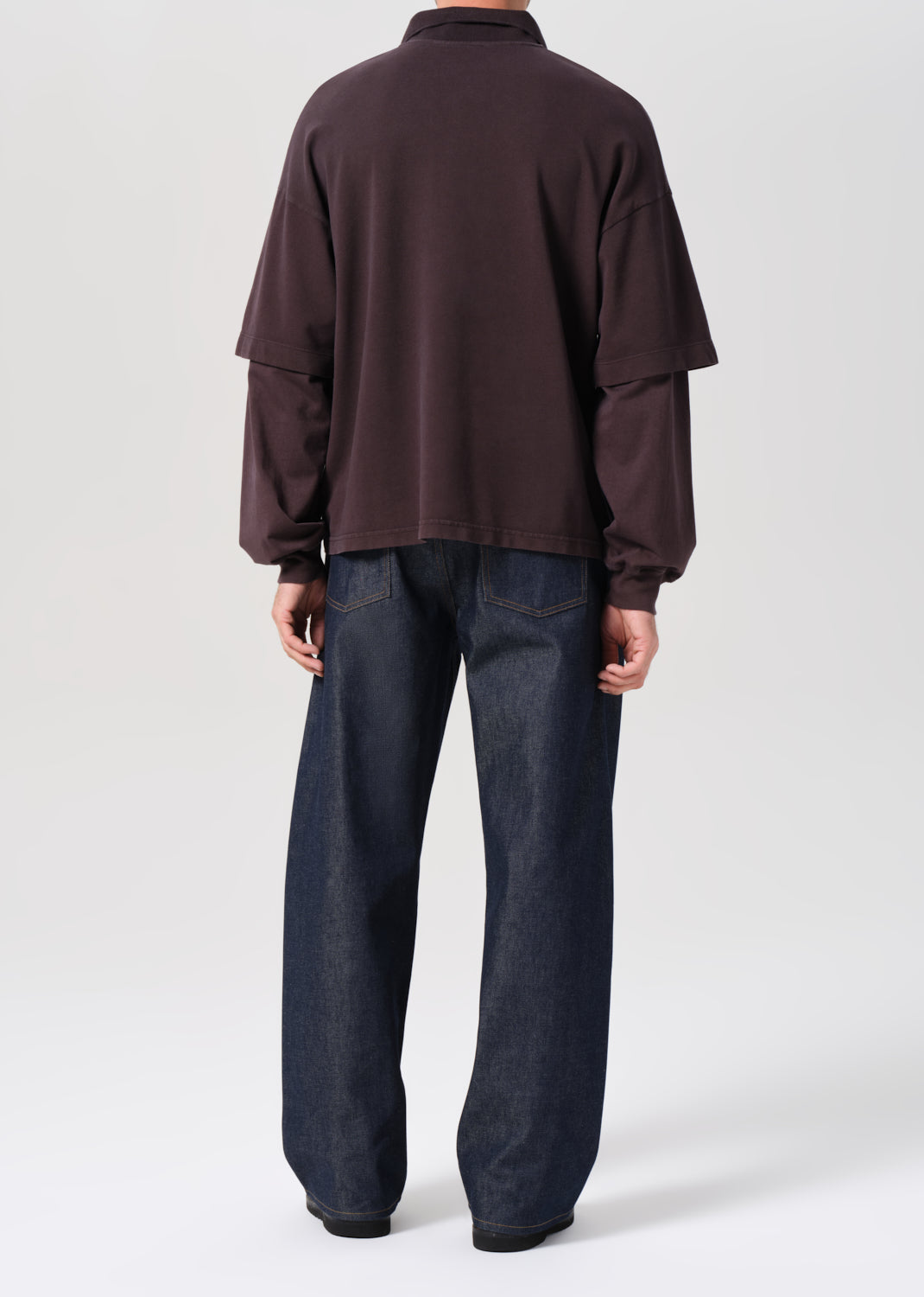 Person wearing a brown long-sleeve shirt and dark blue pants on a white background