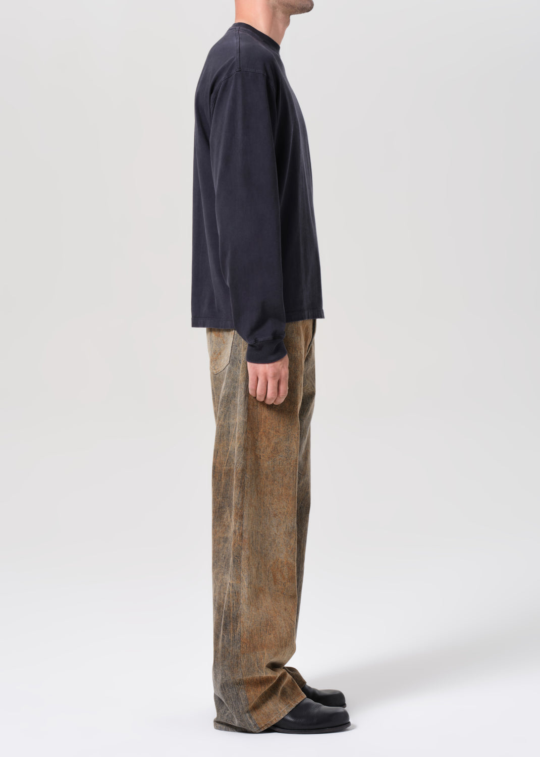 Person wearing a dark long-sleeve shirt and brown pants on a white background