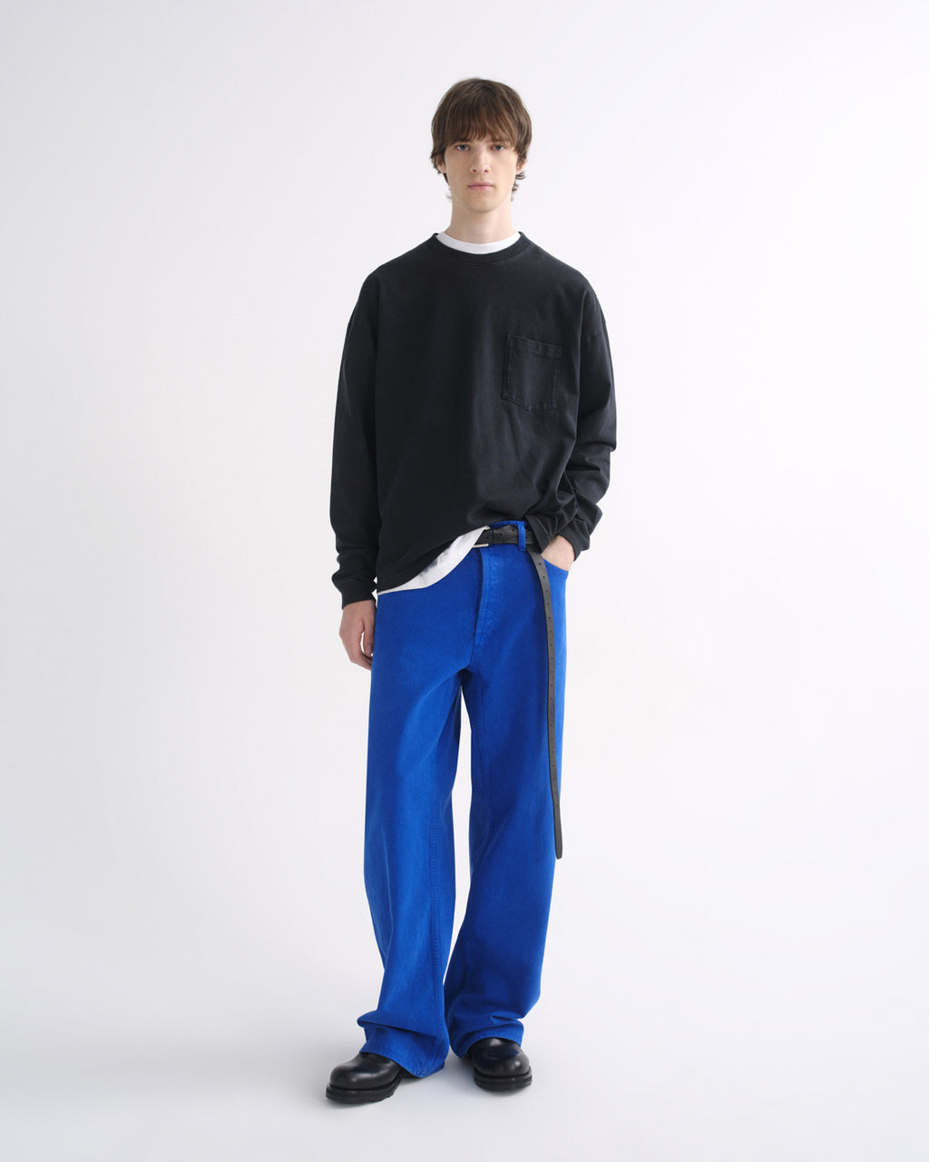 Person wearing a black crewneck sweatshirt with bright blue pants and black shoes on a grey background