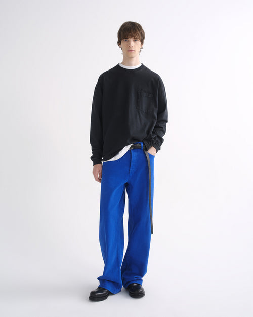 Person wearing a black crewneck sweatshirt with bright blue pants and black shoes on a grey background