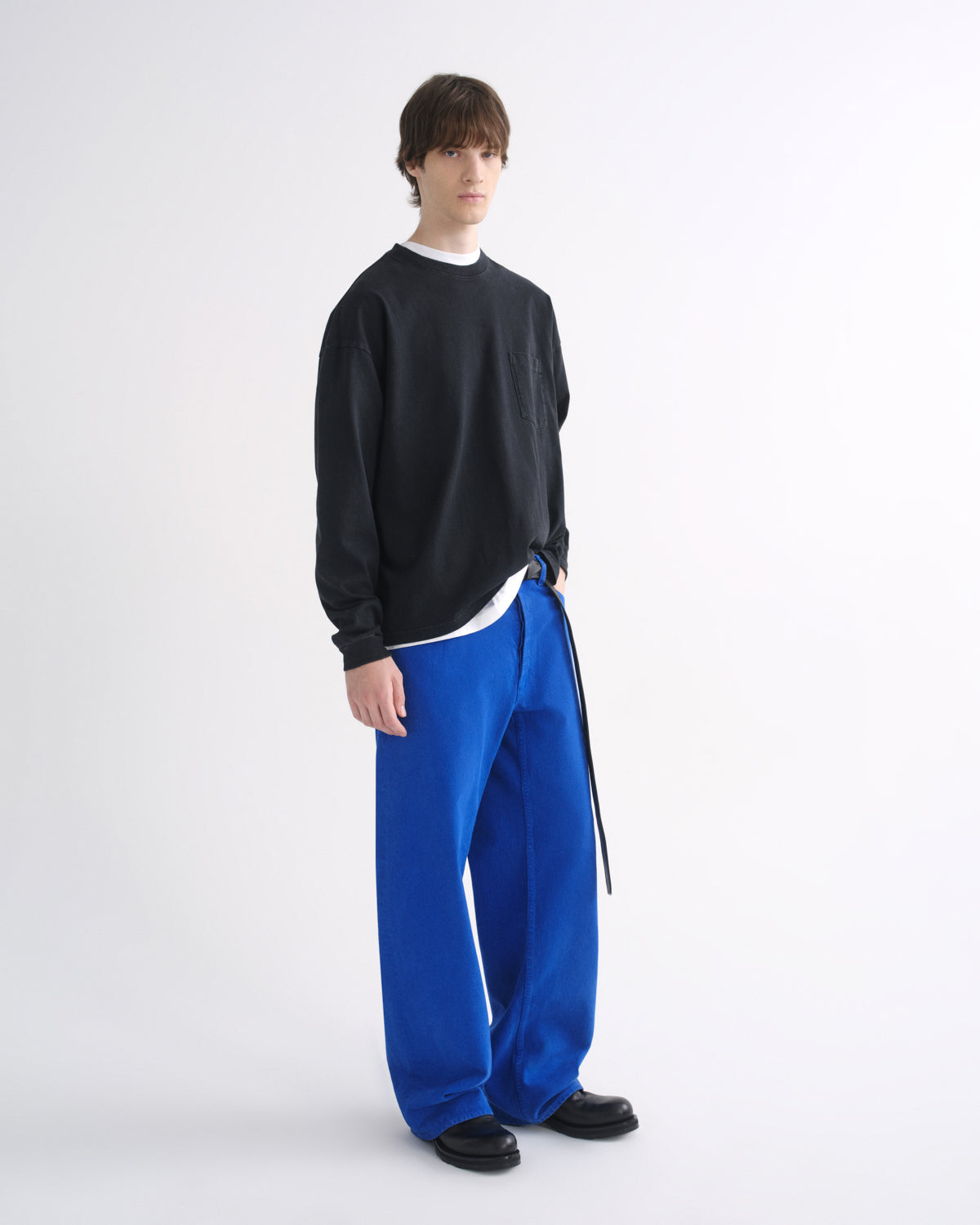 Person wearing a black crewneck sweatshirt with bright blue pants and black shoes on a grey background