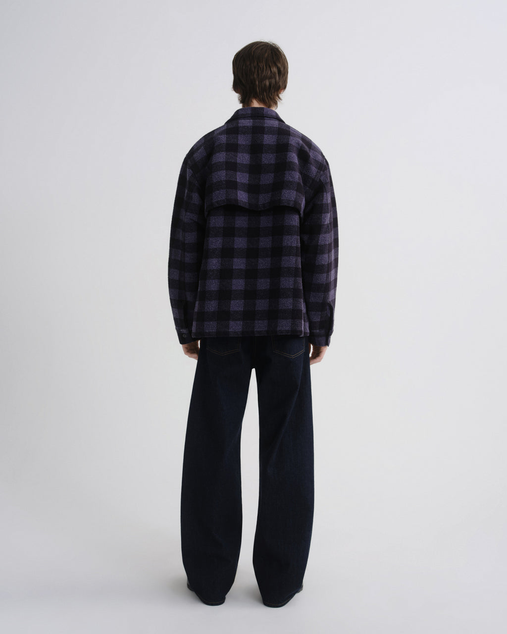 Person wearing a dark plaid shirt and black pants on a white background