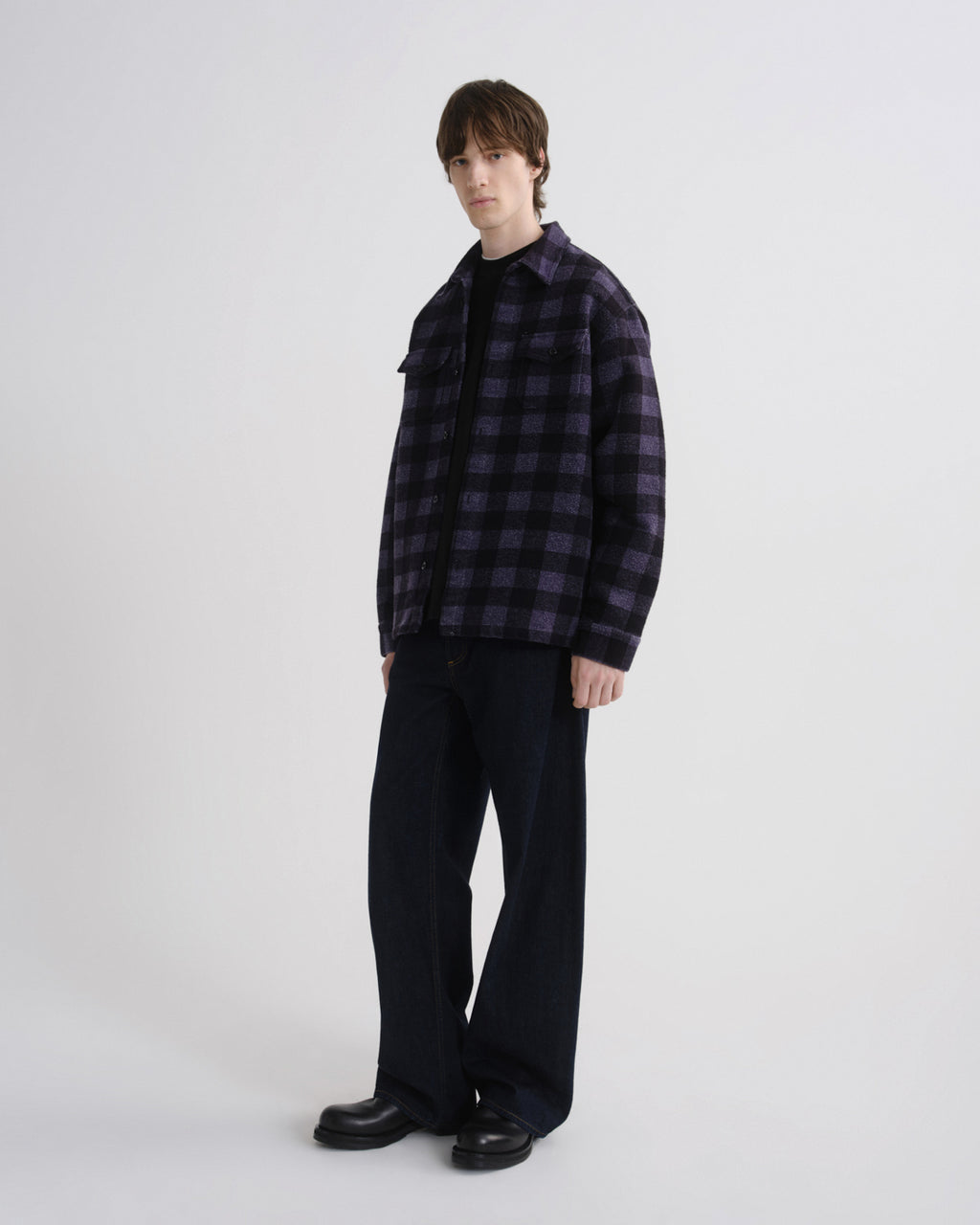 Person wearing a dark plaid shirt and black pants on a white background