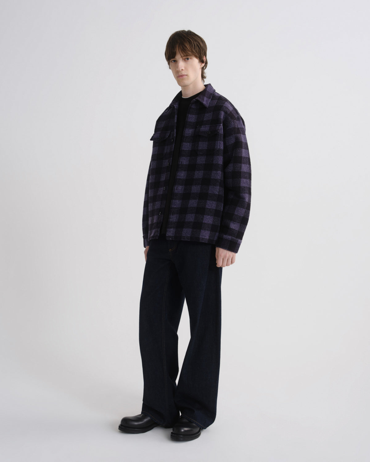 Person wearing a dark plaid shirt and black pants on a white background