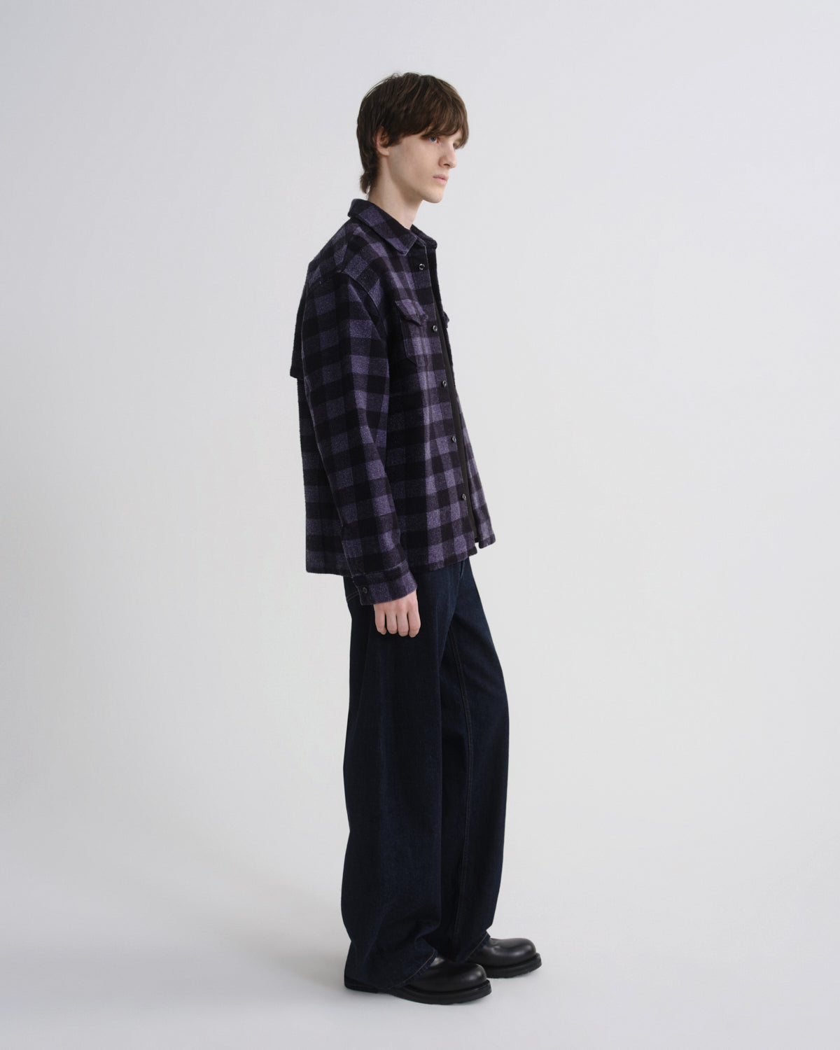 Person wearing a plaid shirt and dark pants on a white background