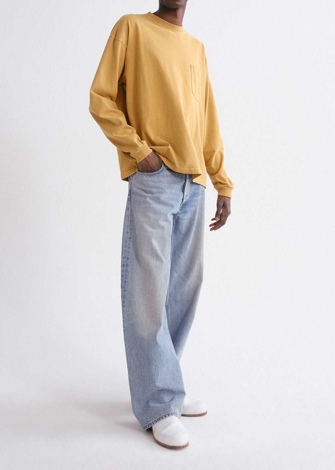 Person wearing a mustard yellow long-sleeve shirt and light blue jeans on a grey background