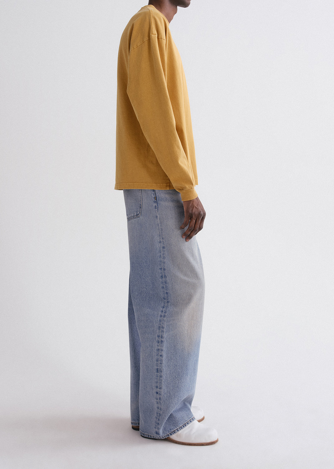 Person wearing a mustard yellow sweater and blue jeans on a grey background