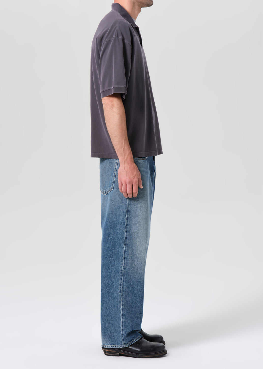 Person wearing a dark gray polo shirt and blue jeans on a white background