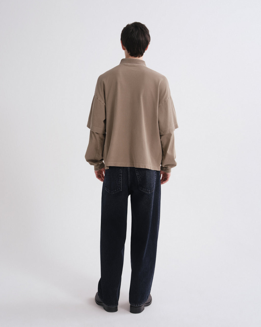 Person wearing a beige shirt and dark jeans on a grey background