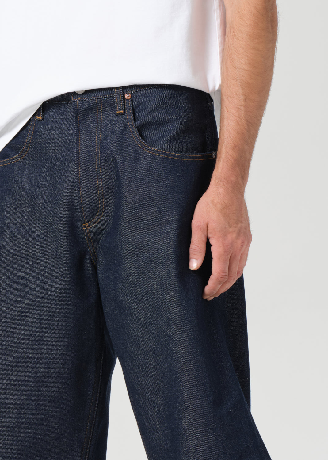 Person wearing dark blue jeans on a plain background