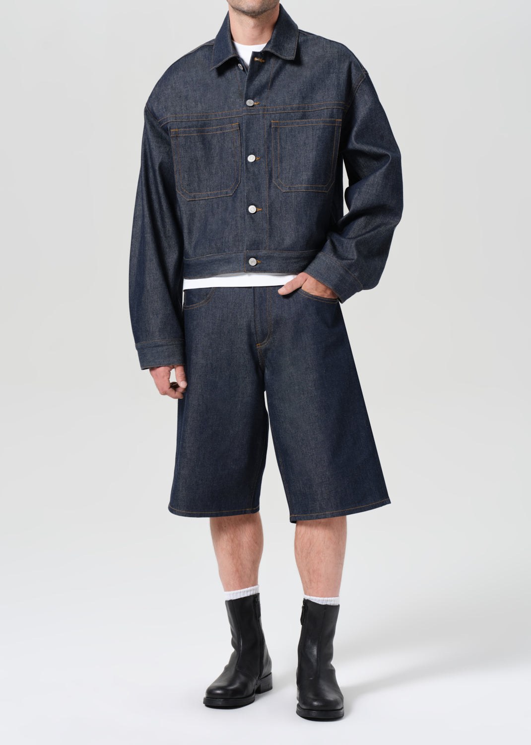 Person wearing a dark denim jacket and shorts on a white background