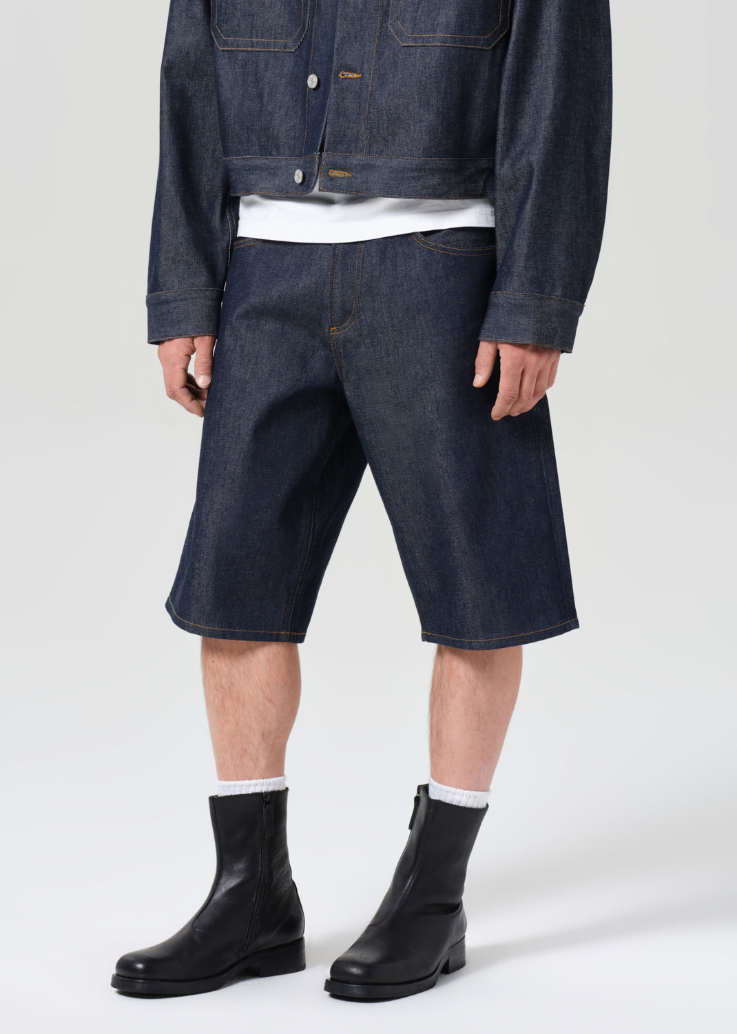 Person wearing dark denim shorts, a jacket, and black boots on a white background