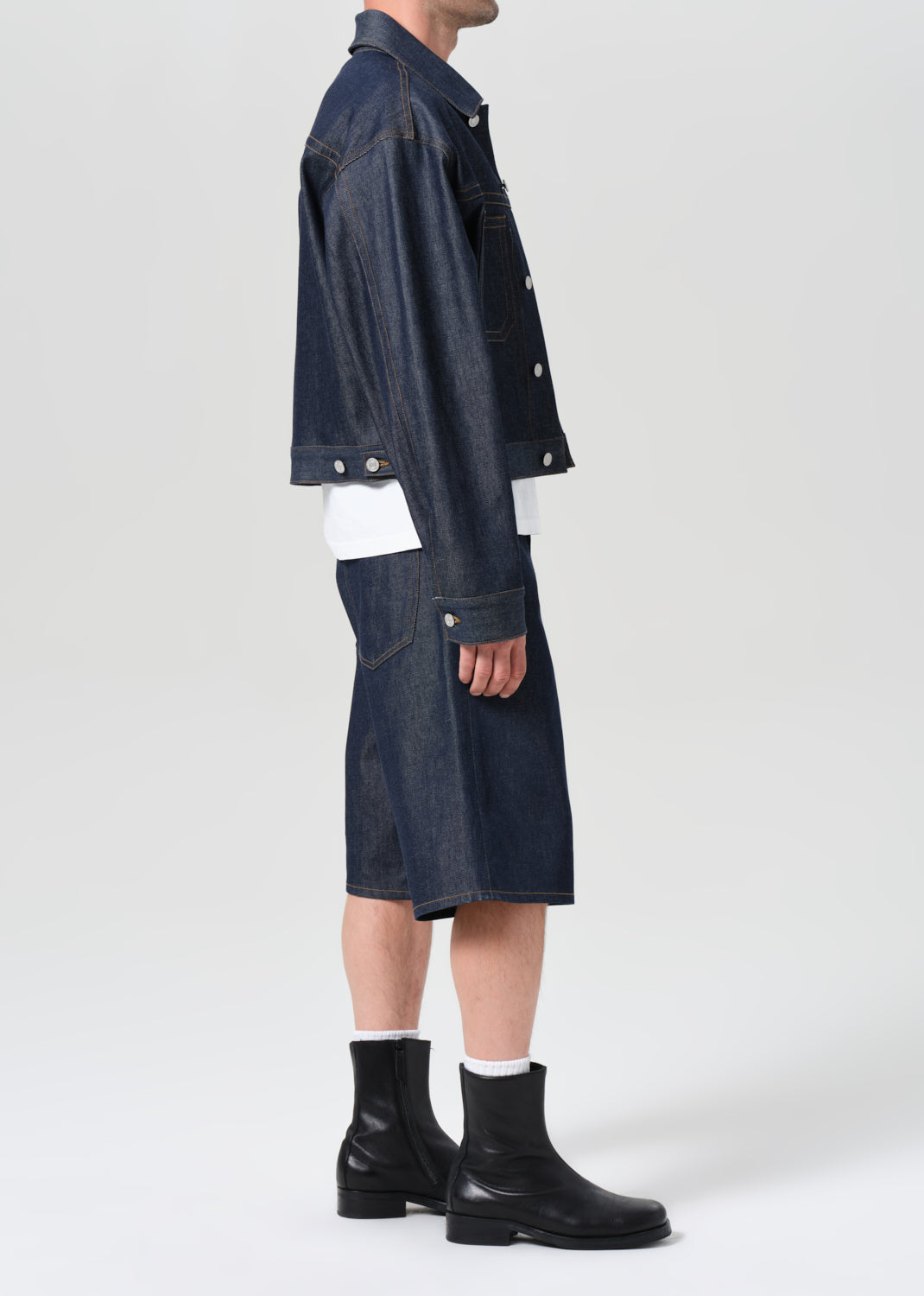 Person wearing a dark denim jacket and skirt with black boots on a white background