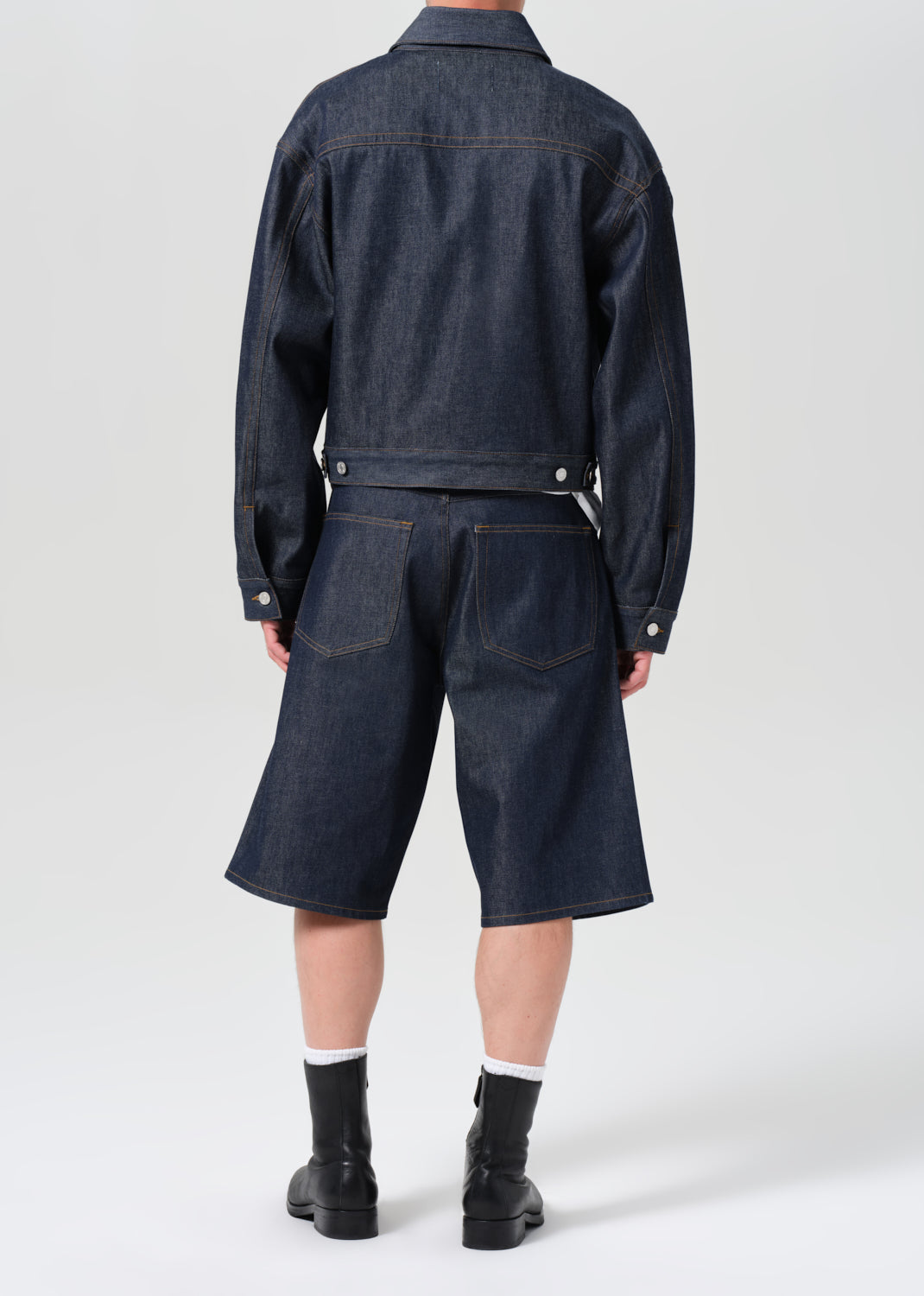 Person wearing a dark denim jacket and shorts on a white background