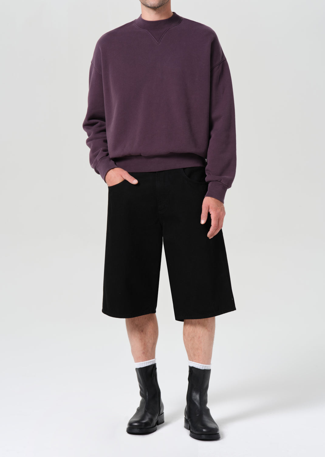 Person wearing a purple sweater, black shorts, and black rain boots on a white background