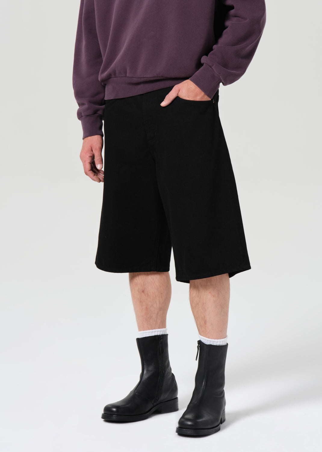 Person wearing a purple sweater, black shorts, and black boots on a white background
