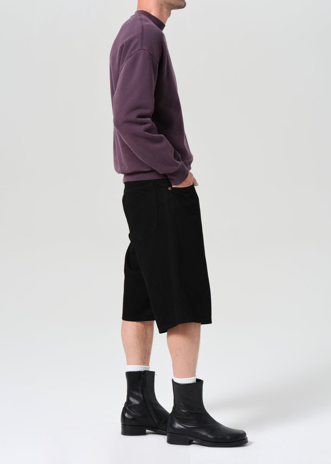Person wearing a purple sweater, black shorts, and black boots on a white background