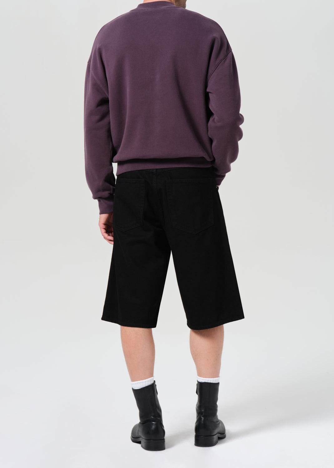 Person wearing a purple sweatshirt and black shorts on a white background