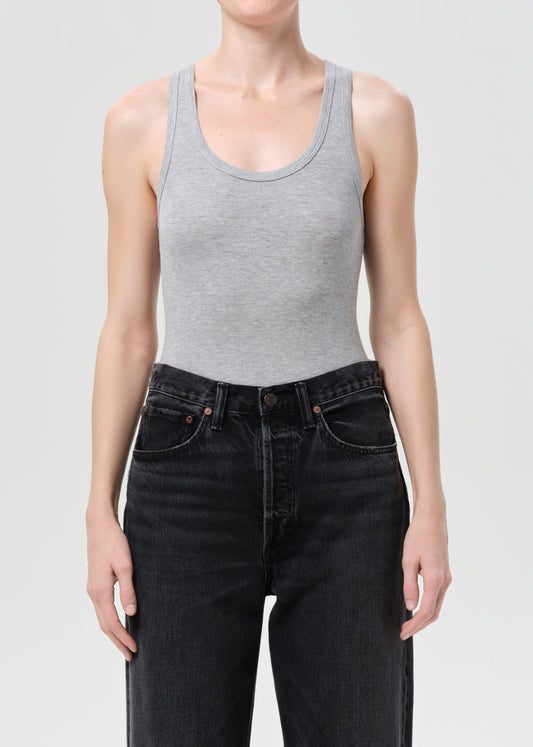 Person wearing a gray tank top and black jeans on a light gray background