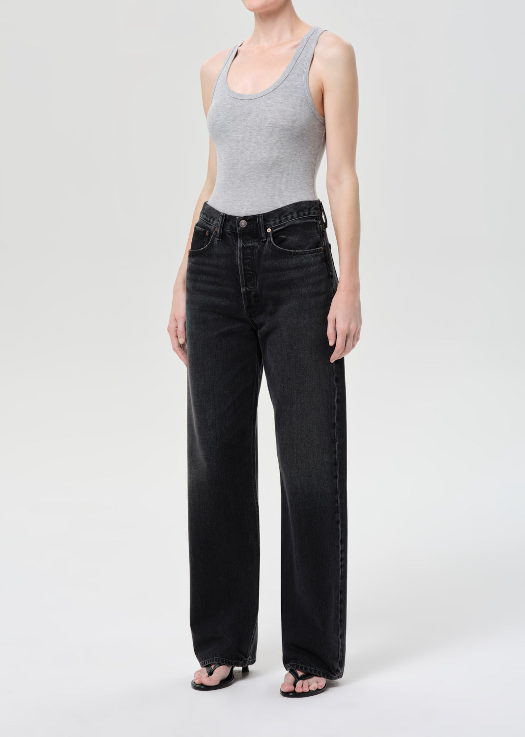 Person wearing a gray tank top and black jeans on a white background