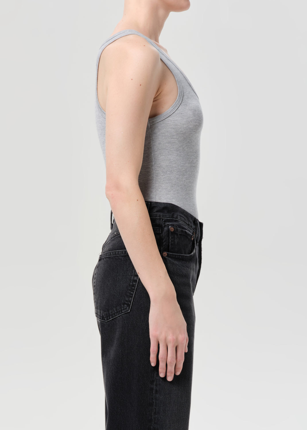 Person wearing a gray tank top and black pants on a light gray background