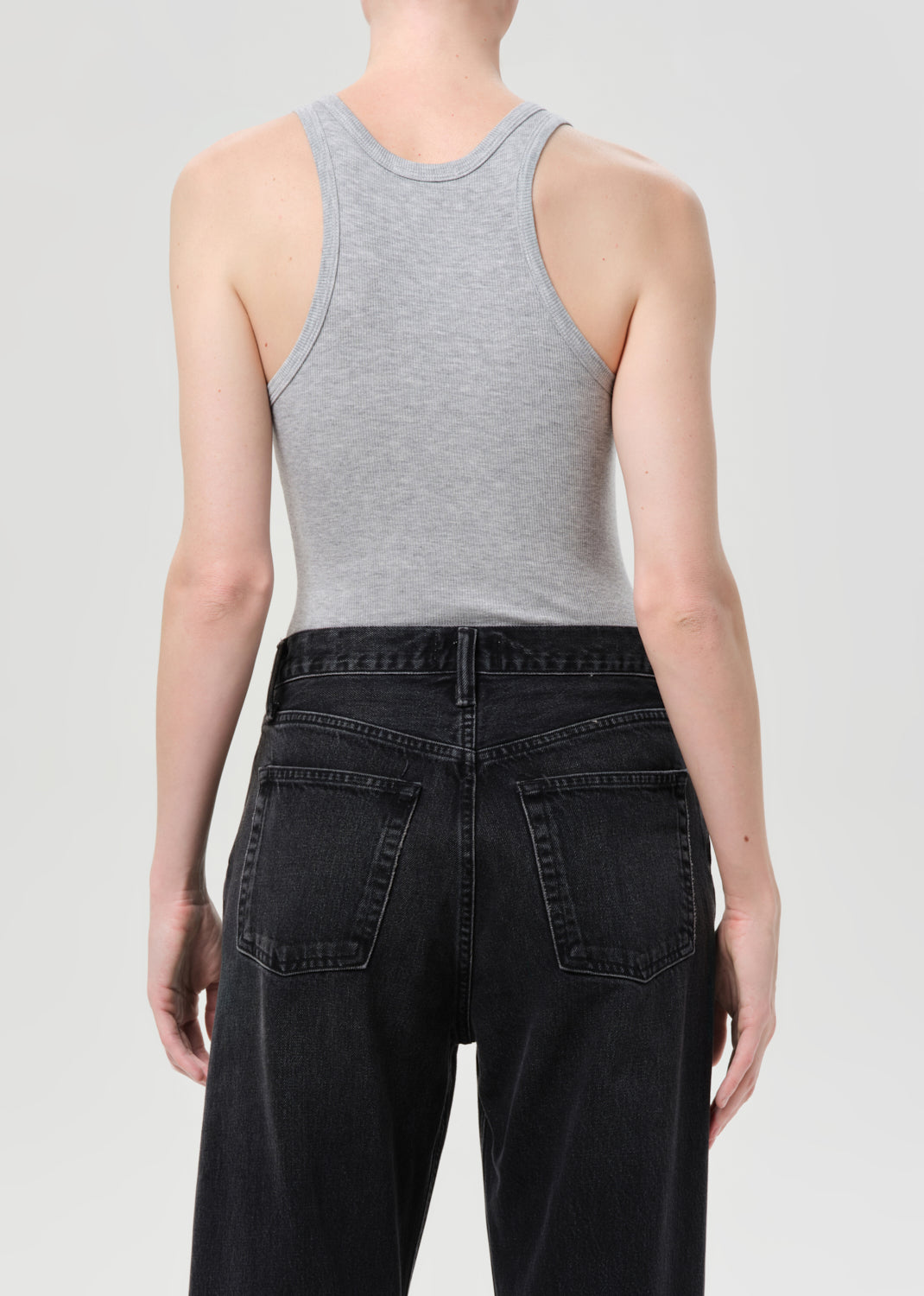 Person wearing a gray tank top and black jeans on a plain background