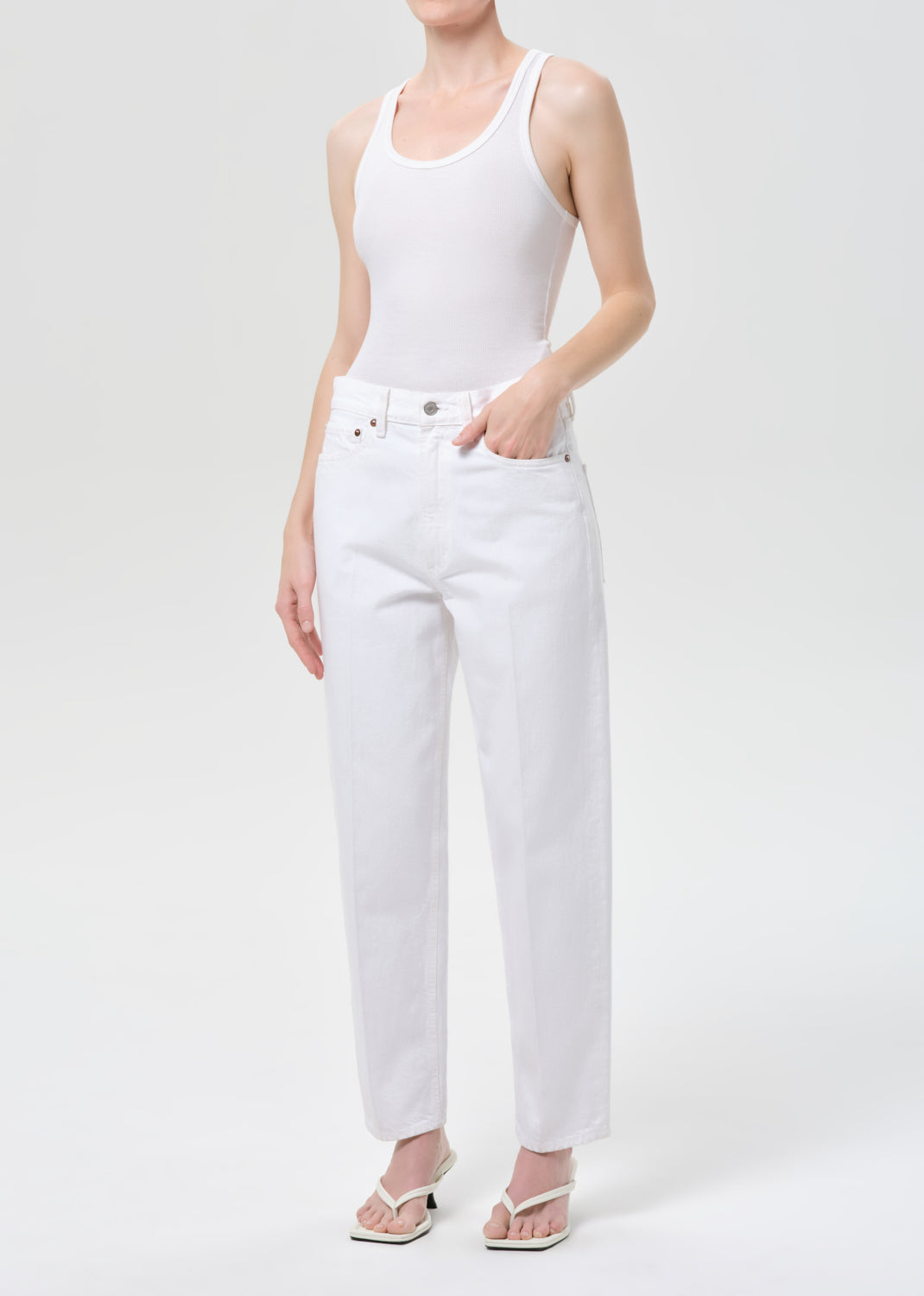 Person wearing a white tank top and white pants on a light gray background